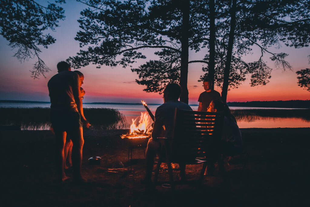 people around a campfire near a lake at sunset