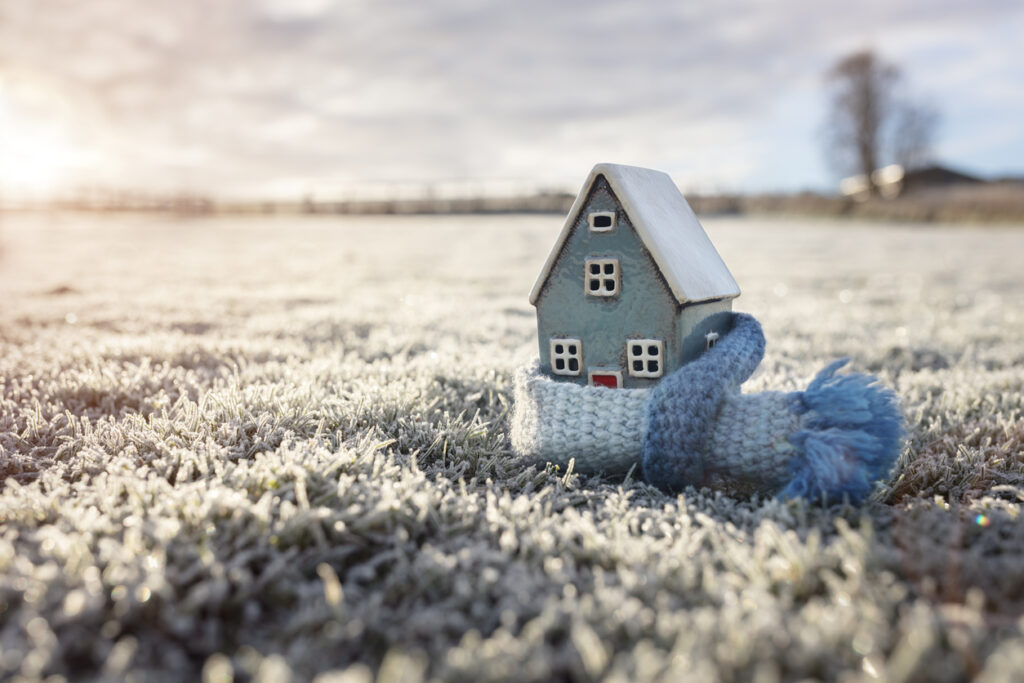 toy house with a scarf wrapped around it, sitting in field of frosted grass