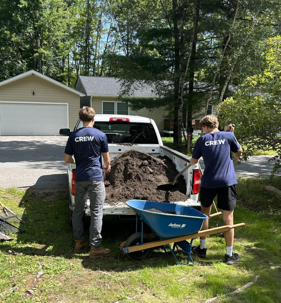 2 young men shoveling dirt from the back of a pickup into a wheelbarrow